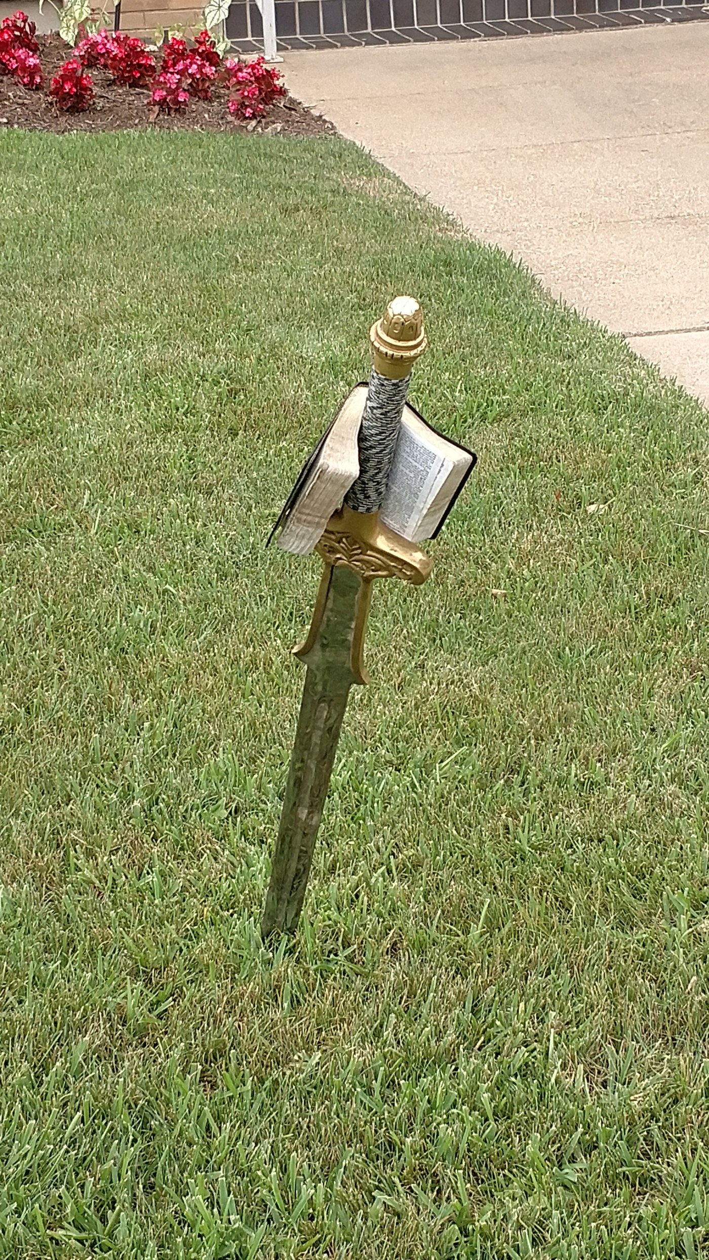 A sword planted in the ground with an open Scripture resting on its hilt